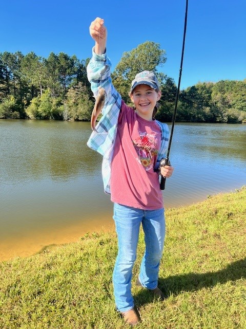 A young girl in a pink shirt holds up her first catch.