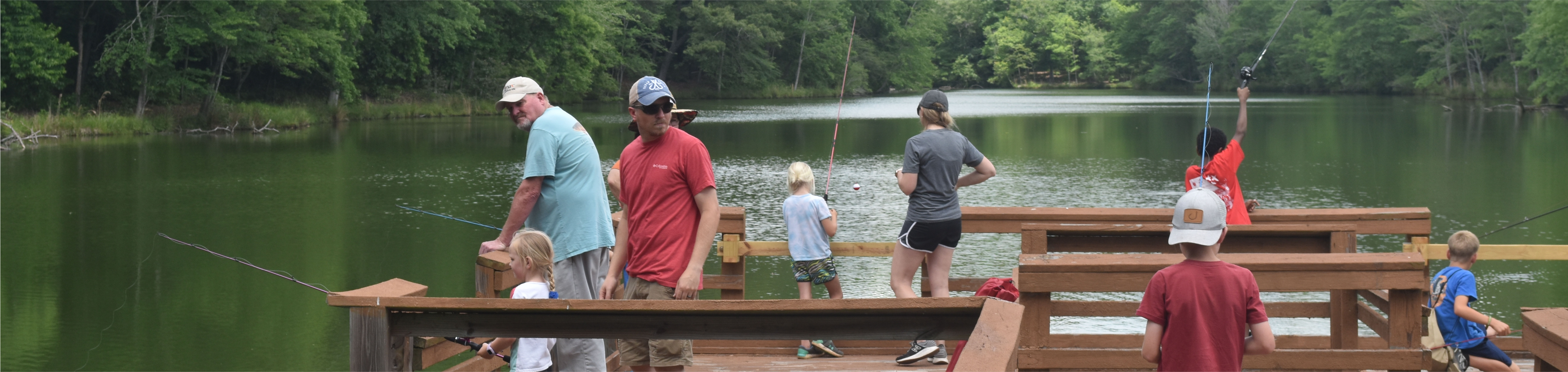 A group of people stand on a peir casting fishing poles.